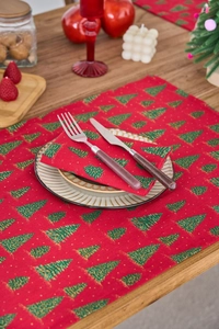 Detail of red Christmas napkin with green tree print and golden accents on wooden table