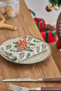 Close-up of festive napkin with green pine and red berry prints on a ceramic plate