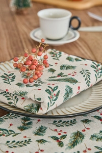 Close-up of a linen Christmas napkin with green pine needles and red berries on a ceramic plate
