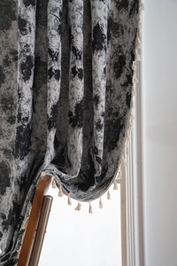 Detail of grey floral jacquard curtain with elegant cream tassels on textured fabric