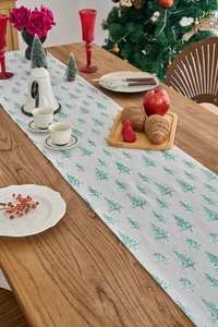 Close-up of a festive table runner with green Christmas tree prints on a wooden table