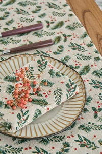 Detailed view of Christmas napkins with pine needles and red berry prints on linen fabric