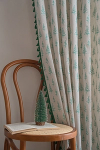 Close-up of cream curtain with green Christmas tree patterns and pom-pom fringe details