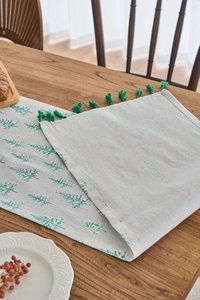 Close-up of beige table runner featuring green Christmas trees and decorative tassels