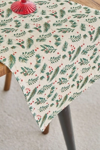 Detail of Christmas table runner with green pine needles and red berries on linen fabric