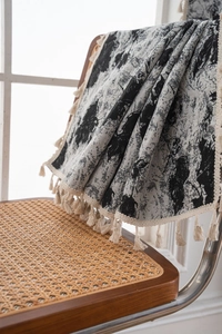 Detail of woven throw blanket with black and white patterns and cream fringe on a chair