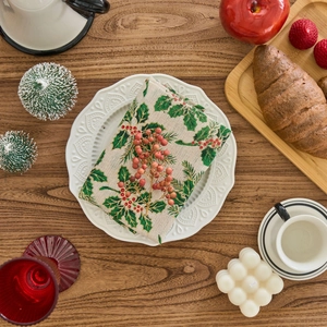 Christmas cloth napkin with holly berry print on a white plate over a wooden table