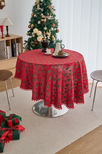Detailed close-up of round red Christmas tablecloth with pine prints and ball fringe