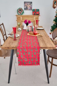 Detailed view of red Christmas table runner with green tree patterns and pompom fringe