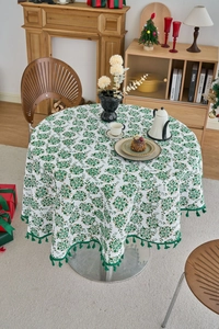 Close-up of a white round tablecloth with green pine branch prints and tassel edges
