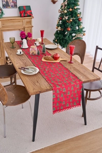 Detail of red Christmas table runner with green tree patterns and decorative pompom fringe