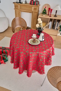 Detail of red Christmas tablecloth with green pine tree prints and red pompom fringe edges