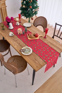 Detail of red Christmas table runner with green tree patterns and decorative fringe