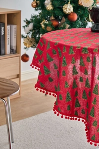 Close-up of red Christmas tablecloth with green pine prints and red pom-pom fringe edges