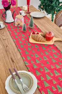 Detail of red Christmas table runner featuring green tree prints on wood dining table