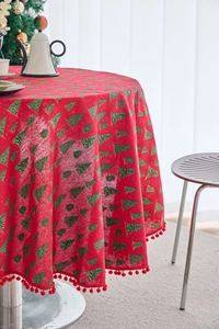 Macro shot of red Christmas round tablecloth with green pine tree prints and pom-pom edge