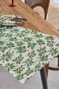 Close-up of linen napkin with Christmas holly leaf and red berry print on wood table