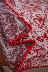 Close-up of red bird and floral jacquard tablecloth with festive pom-pom lace edge