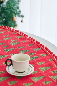 Detail of red Christmas table runner with green tree prints and plush pom-pom trim edges