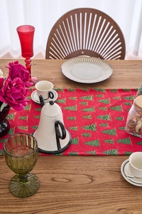 Detail of red Christmas table runner with green gold-stamped trees on a wooden table