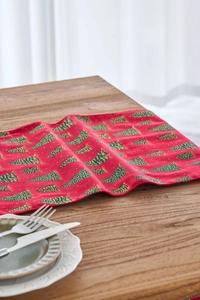 Close-up of red Christmas table runner with green tree prints on wooden table