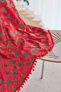 Detail of red Christmas tablecloth with pine tree prints and festive pom-pom edge