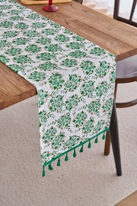 Detail of green and gold floral pattern table runner with green tassel on dark wood table