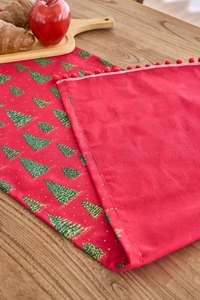 Close-up of red Christmas table runner with gold tree prints and decorative pom-poms