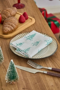 Close-up of linen napkin with green Christmas tree prints on a rustic wooden table