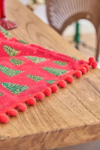 Detail of red Christmas table runner featuring green tree print and festive pom-pom edges