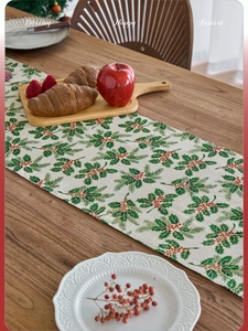 Close-up of Christmas table runner with holly leaf patterns on a wooden table surface