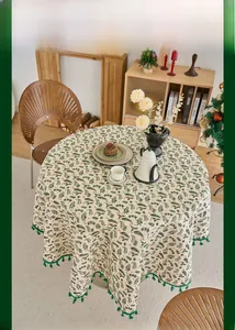 Detailed close-up of a round Christmas tablecloth with pine motifs and green fringe tassels