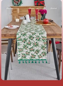 Detail of Christmas table runner with holly patterns, red berries and green tassel fringe