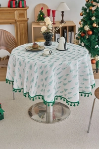 Detail of round Christmas tablecloth featuring green pine prints and elegant fringe edges