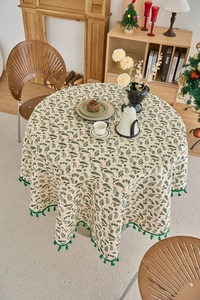Detail of Christmas round tablecloth with green pine needles, red berries and fringe trim
