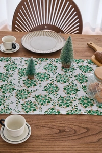 Detail of green and gold poinsettia print on a white festive table runner with linen texture