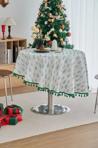 Detail of round Christmas tablecloth with green pine tree patterns and fringe trim