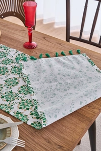 Detail of green floral table runner with elegant tassels on a dark wood dining table