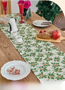 Detail of Christmas table runner with green holly leaf and red berry print on linen fabric