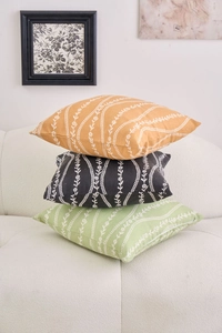 Modern floral throw pillow covers in yellow, black, and green stacked on a cozy sofa