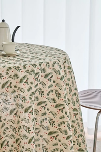 Detail of round Christmas tablecloth with pine needle and red berry print on beige linen