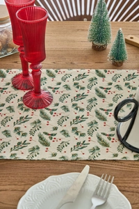 Detail of Christmas table runner with pine branches and red berries on a wooden table