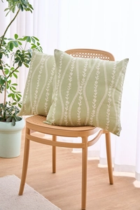 Close-up of light green floral cushion covers with white wave patterns on a woven chair