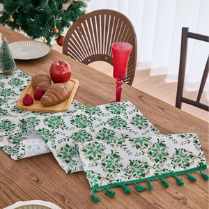 Green and gold floral Christmas table runner with tassels on a wooden dining table