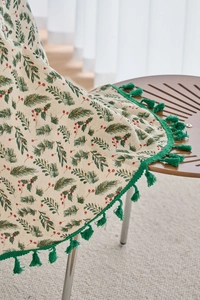 Detailed close-up of pine needle and red berry print tablecloth with green fringe trim