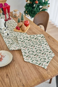 Detail of Christmas table runner with green pine needles and red berries on beige linen