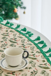 Close-up of festive tablecloth with pine branch patterns and green fringe tassels