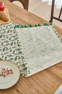 Dettaglio di stampa agrifoglio verde su runner da tavola crema con nappe decorative
