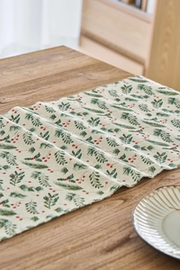 Detail of linen Christmas table runner with green pine needles and red berries patterns