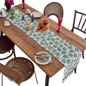 Green floral table runner with tassels on a wooden dining table for home decoration